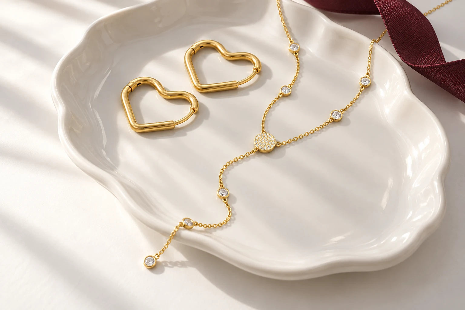Gold heart hoops and a drop necklace arranged on a white jewellery dish