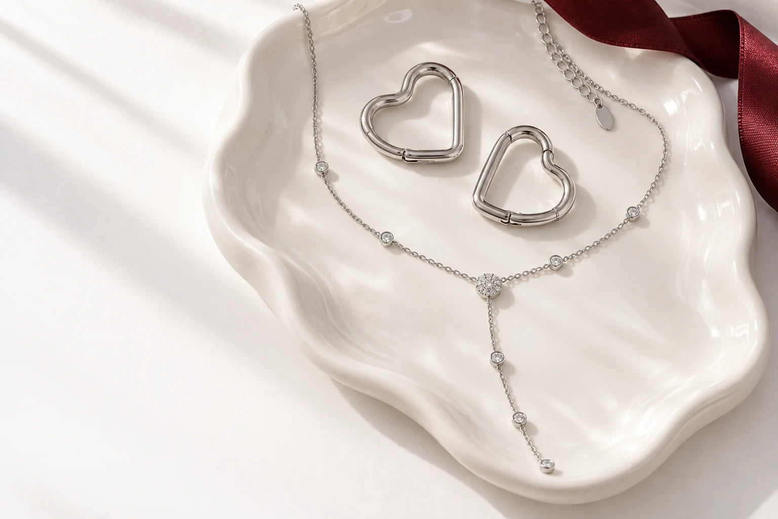 Silver heart hoops and a drop necklace arranged on a white jewellery dish